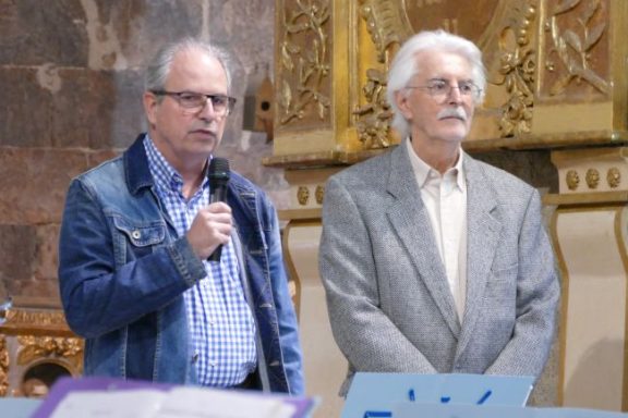 Deux hommes en tenue décontractée, discutant devant un auditoire dans une église.